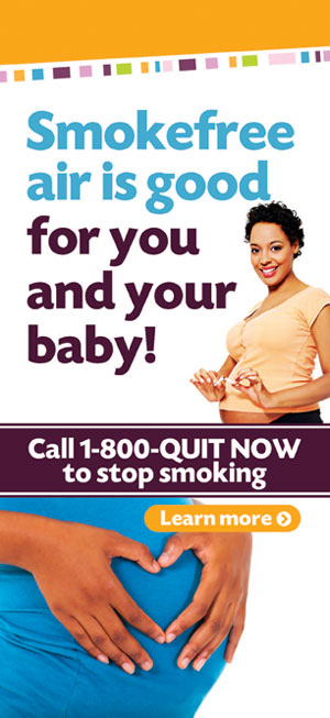 A woman is holding her baby in front of an advertisement.